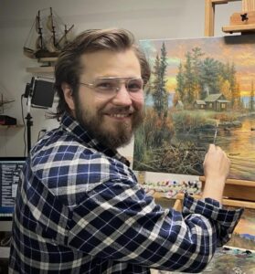 Abraham Hunter sits in front of an easel with his latest work
