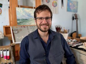 Abraham smiling in front of an easel in his studip